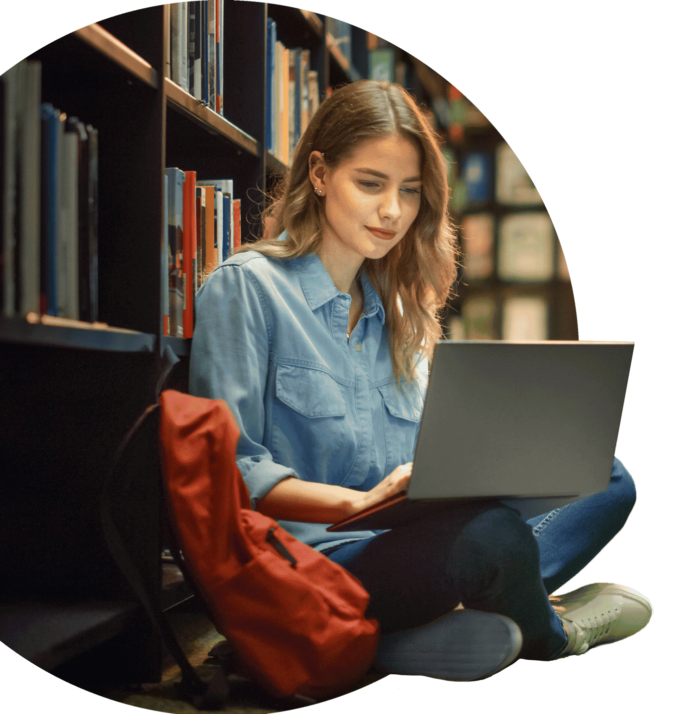 woman sitting against a library shelf with her backpack and laptop